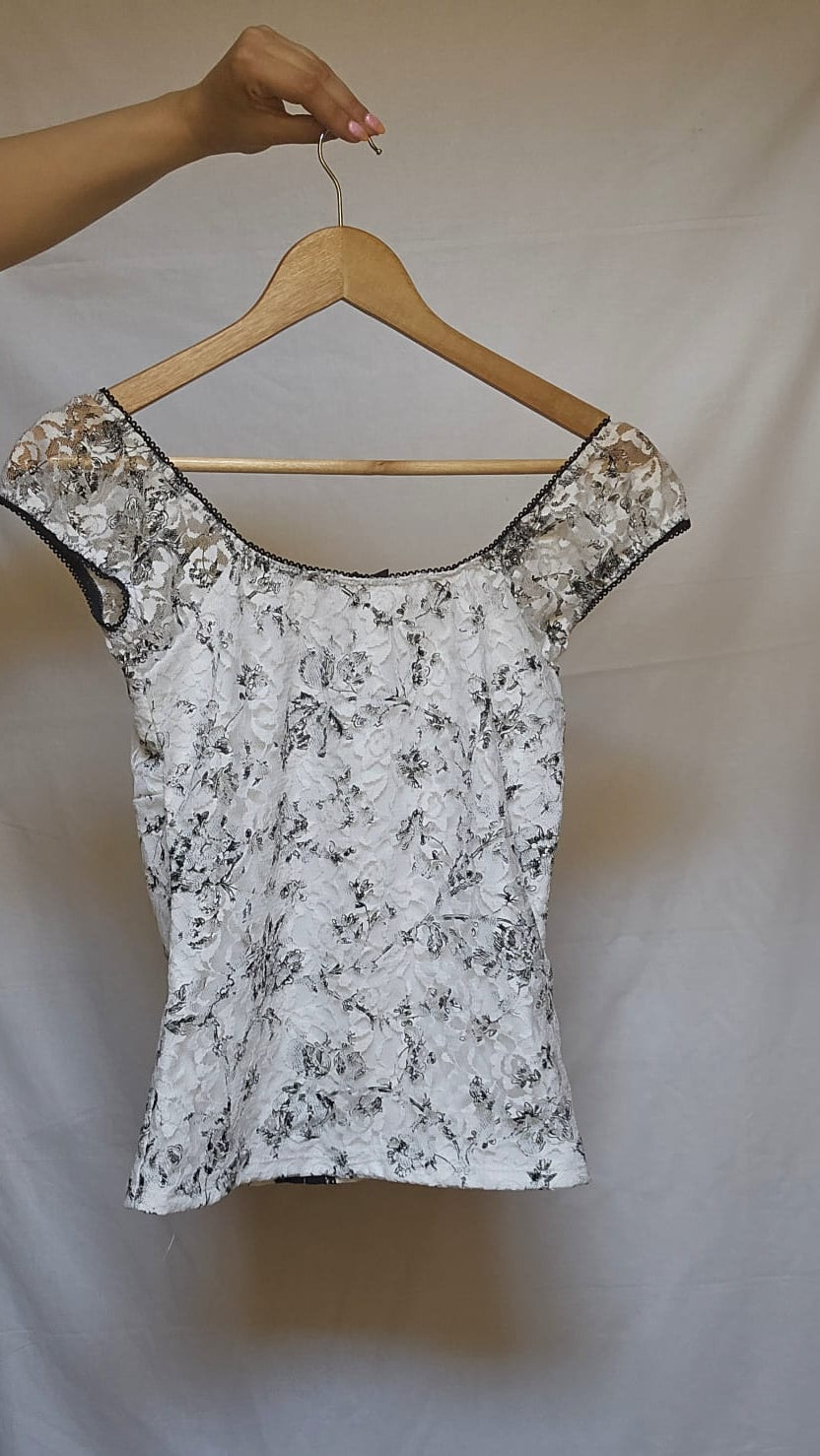 White floral top on a wooden hanger against a plain background