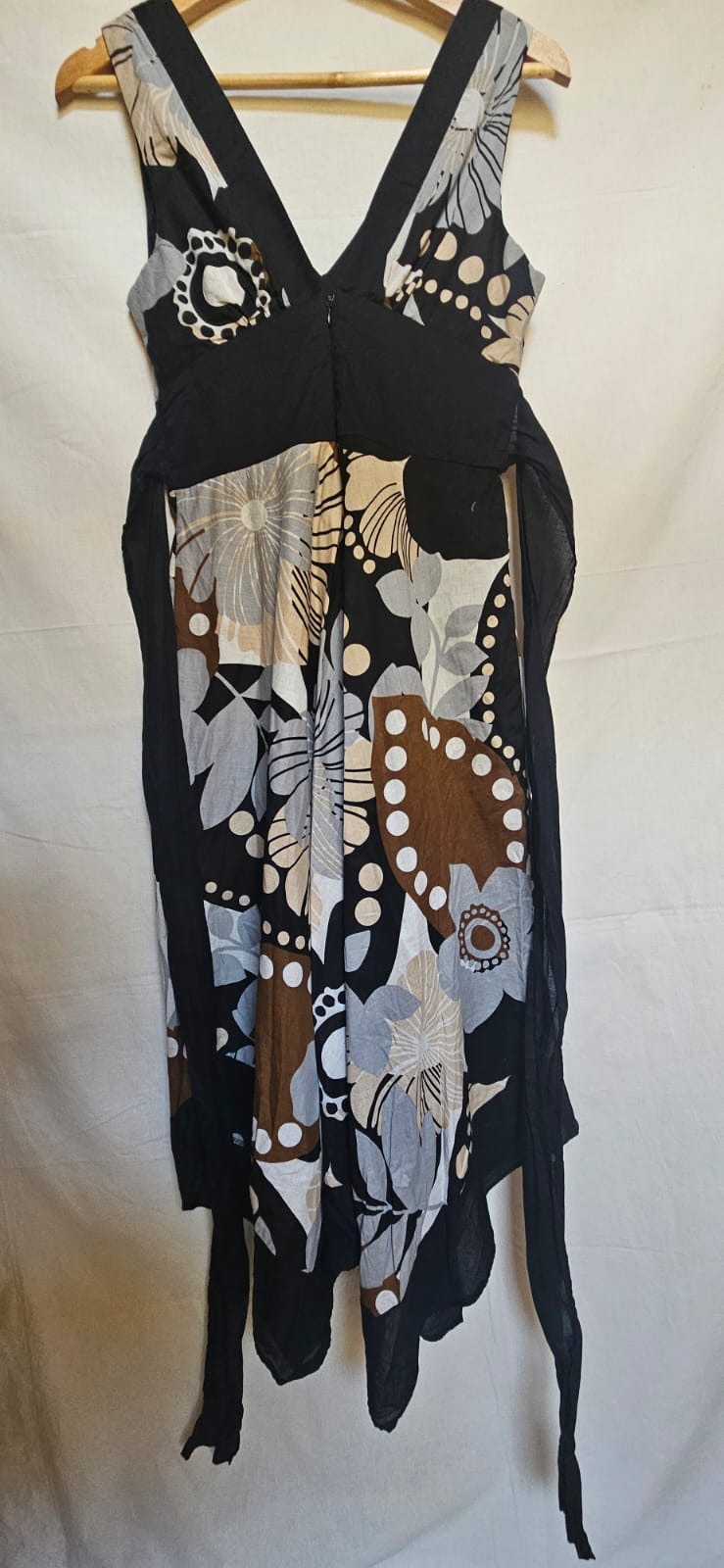 Black dress with floral patterns on a wooden hanger against a white background