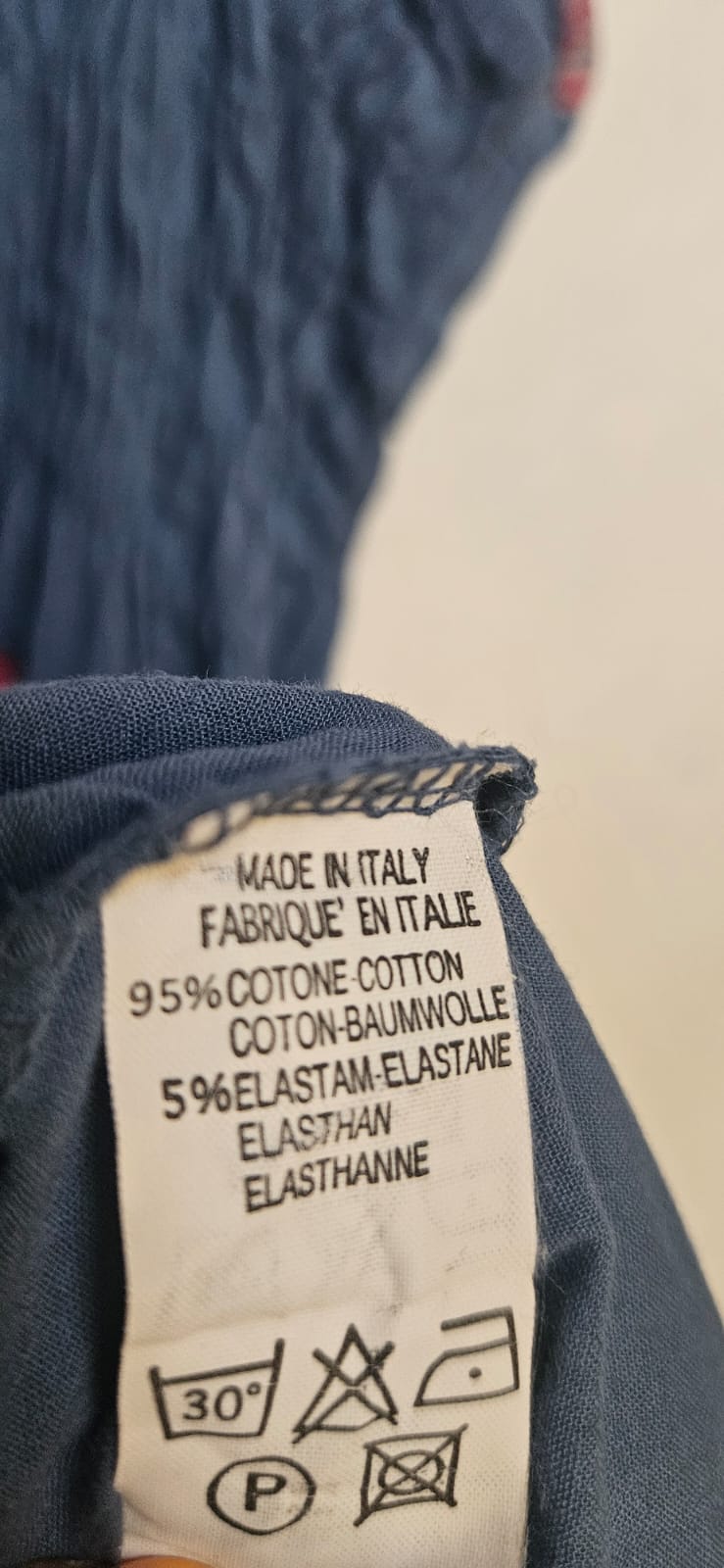 Clothing label on a blue fabric background with text and symbols.