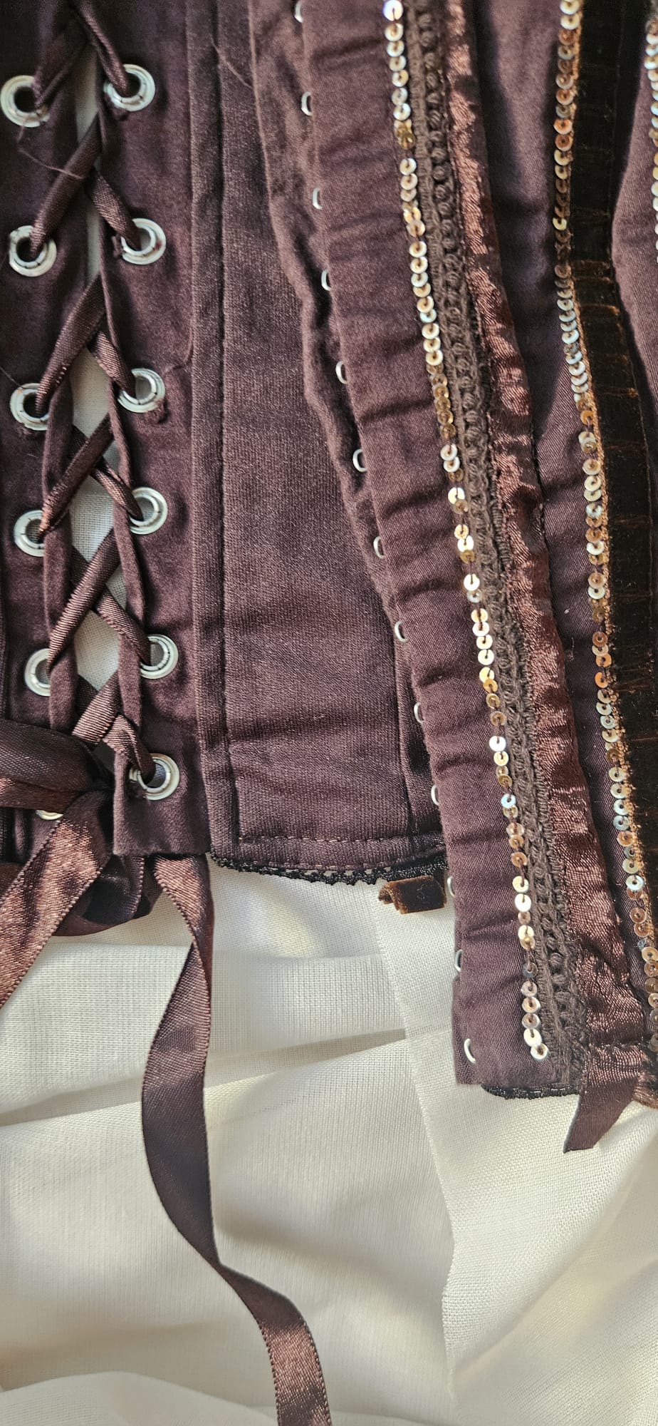 Close-up of a brown garment with lace-up details and decorative trim on a beige background
