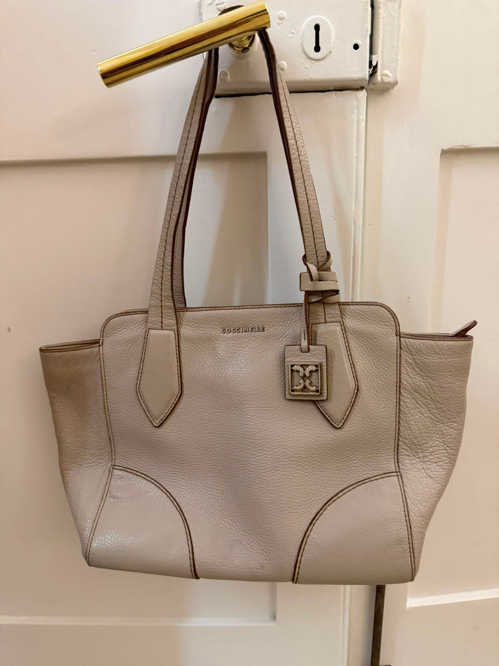 Coccinelle taupe leather tote bag hanging on door handle