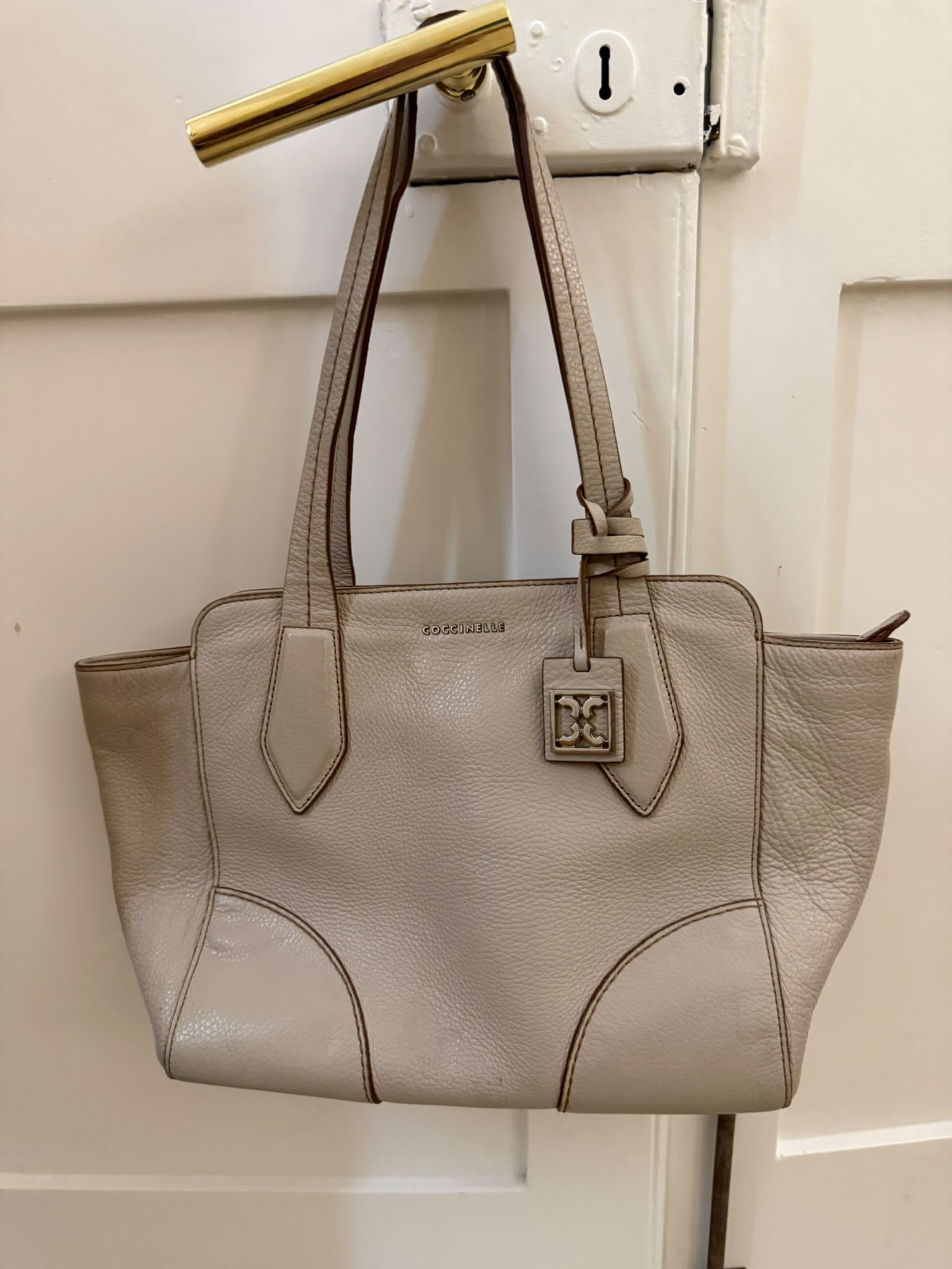 Coccinelle taupe leather tote bag hanging on door handle
