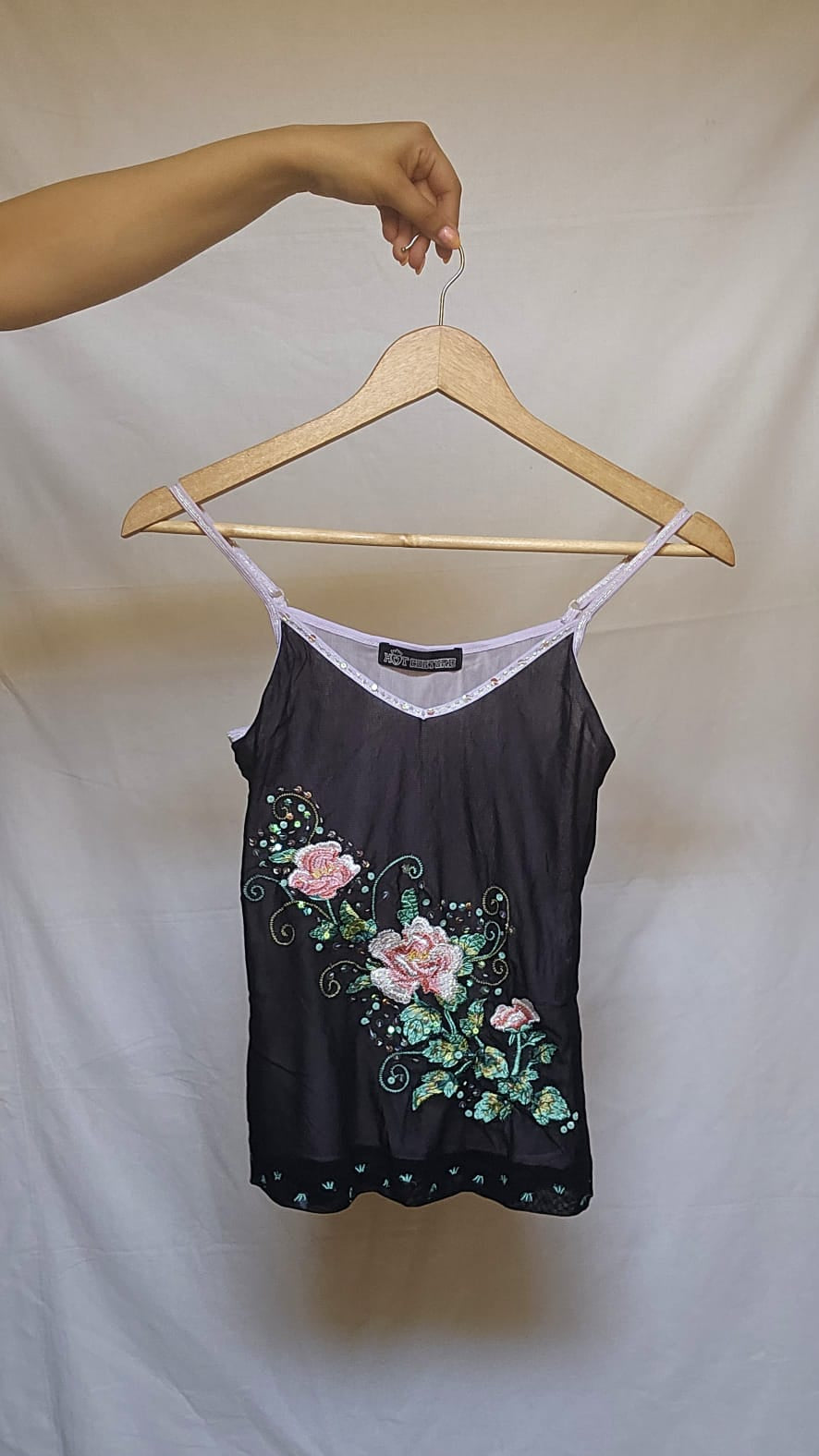 Black tank top with floral embroidery on a hanger against a white background