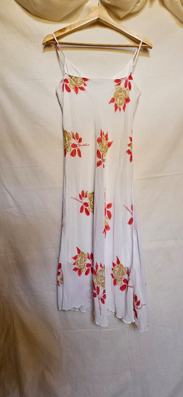 White dress with red floral patterns on a hanger against a beige background