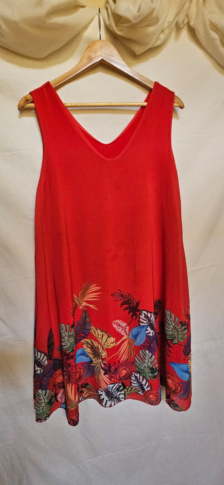 Red sleeveless top with colorful floral patterns on a hanger against a white background