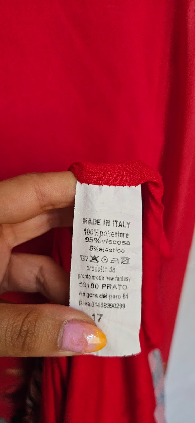 Close-up of a red dress with a label held by a hand.
